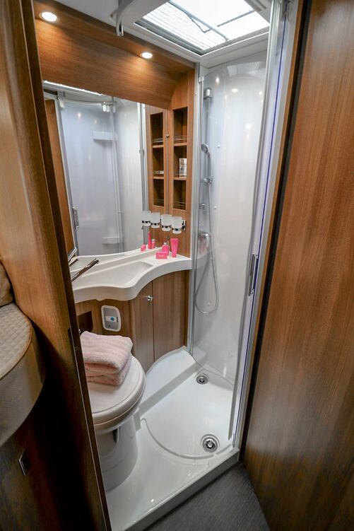 Gefallen kann der Sanitärraum mit seiner holzfarbenen Einrichtung und der ausreichenden Bewegungsfreiheit, wobei auch die mittels Acrylglastüren abteilbare Dusche genug Platz bietet.
